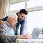 Companion caregiver and senior man using laptop