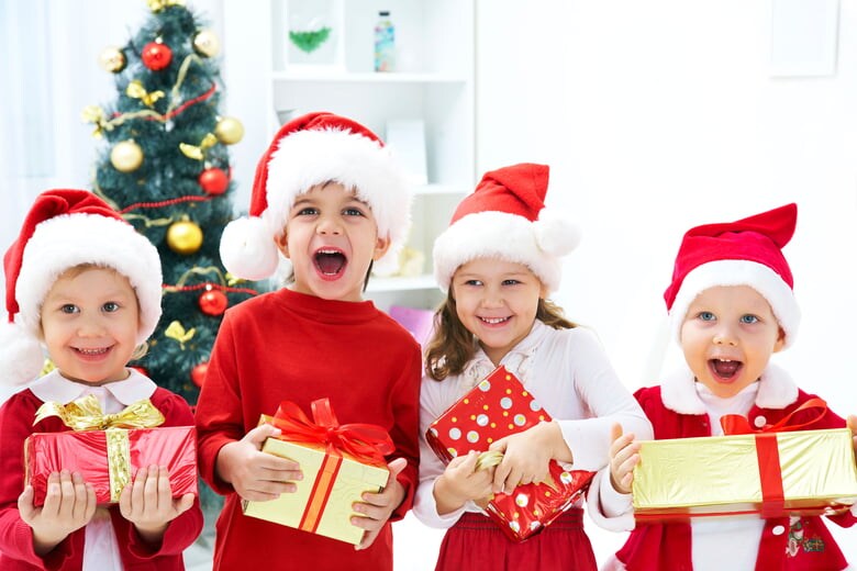 Four young children holding Christmas presents and wearing Santa hats 