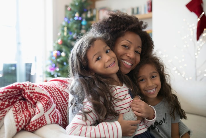 Portrait smiling mother and daughters hugging in living room