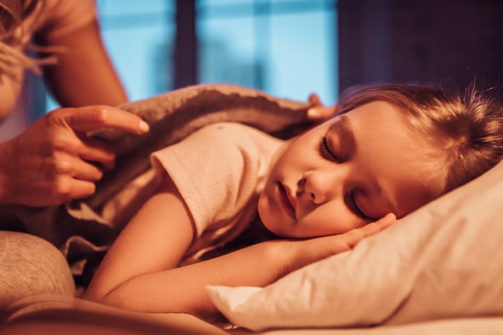 A young girl falls asleep as her night nanny covers her with a duvet 